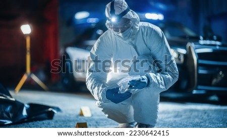 Portrait of Two Forensics Experts Doing Fieldwork at Night at a Crime Scene. One Technician Packs the Bloodied Knife as Murder Weapon While the Other is Taking Photos of the Dead Body.