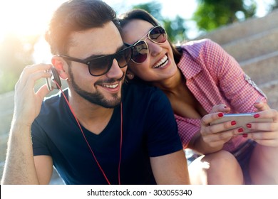 Portrait of two friends using mobile phone and listening to music in the street. - Shutterstock ID 303055340