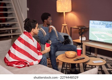 Portrait of two friends watching sports match on TV in living room and drinking beer - Powered by Shutterstock