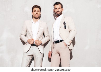 Portrait Of Two Handsome Confident Stylish Hipster Lambersexual Models. Sexy Modern Men Dressed In White Same Elegant Suit. Fashion Male Posing In Studio Near Grey Wall