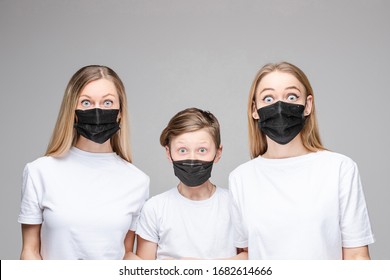 Portrait Of Two Handsome Girls With Long Fair Hair And A Young Boy With Black Medical Masks On Their Faces Isolated On Grey Background