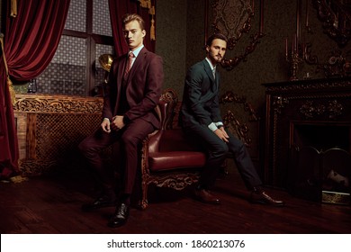 Portrait Of Two Handsome Young Men In Elegant Classic Suits Posing In A Luxury Apartments With Classic Interior. Men's Beauty, Fashion.