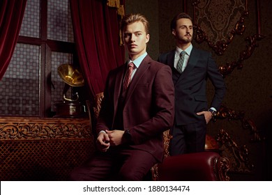 Portrait of two handsome young men in elegant classic suits posing in a luxury apartments with classic interior. Men's beauty, fashion.