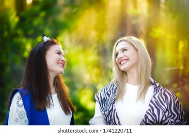 Portrait Of Two Happy Caucasian Women, Blonde And Brunette, Talking And Smiling In Sunset Time In Sunny Park. Horizontal Shape, Copy Space. Time Together After Selfisoltion. Friends Meeting.