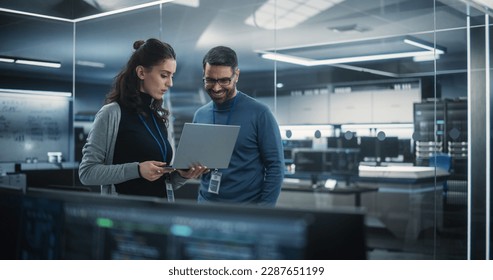 Portrait of Two Happy Female and Male Engineers Using Laptop Computer to Analyze and Discuss How to Proceed with the Artificial Intelligence Software. Casually Chatting in High Tech Research Office