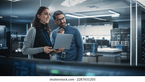 Portrait of Two Happy Female and Male Engineers Using Laptop Computer to Analyze and Discuss How to Proceed with the Artificial Intelligence Software. Casually Chatting in High Tech Research Office - Powered by Shutterstock