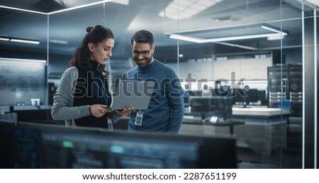 Portrait of Two Happy Female and Male Engineers Using Laptop Computer to Analyze and Discuss How to Proceed with the Artificial Intelligence Software. Casually Chatting in High Tech Research Office