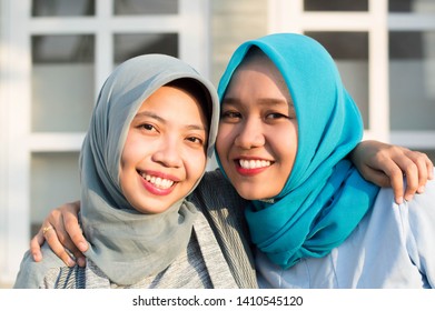 Portrait of two happy hijab women, smiling at the camera while embracing in front of their house on a sunny day - Shutterstock ID 1410545120