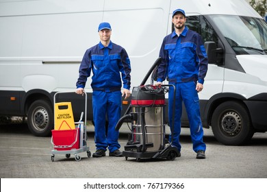 Portrait Of Two Happy Male Janitors Standing With Cleaning Equipment