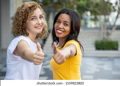 Portrait of two happy multiethnic women giving thumb up gesture; caucasian woman with african woman showing good, yes, accepting, positive, deal endorsing thumb up gesture