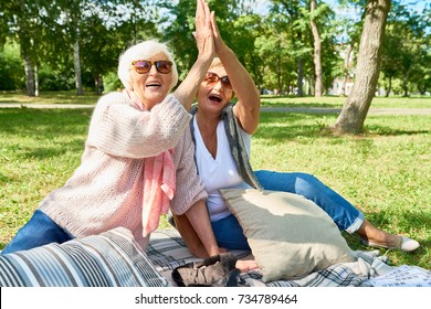 Portrait of two happy senior woman doing high five enjoying picnic in park on sunny autumn day - Powered by Shutterstock