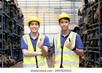 Portrait of two happy smiling Asian industrial engineer worker men with safety vest and helmet giving thumbs up to camera at manufacturing plant factory with many engine parts as blurred background. - Powered by Shutterstock