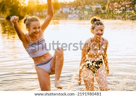Portrait of a two happy teenager girls splashing in the water on a sunny summer day. Girls friends enjoys a summer holiday on the lake shore. Active holidays. Vacation on sea or river. Dynamic image.