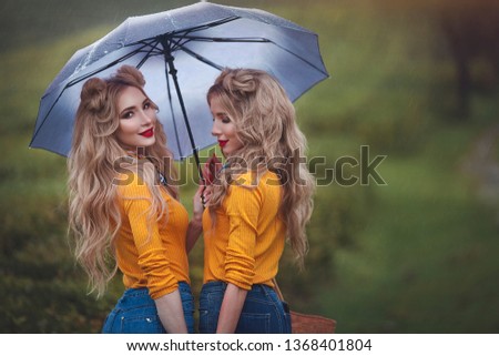 Portrait of Two happy twin girls walking under an umbrella on tea plantations. Young women blonde twins in pin up style.