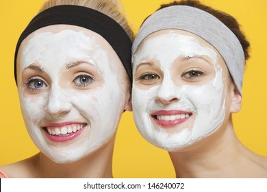 Portrait Of Two Happy Women With Face Pack On Their Faces Over Yellow Background