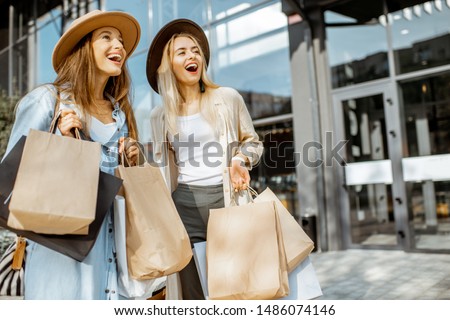 Portrait of a two happy women with shopping bags, standing together in front of the shopping mall