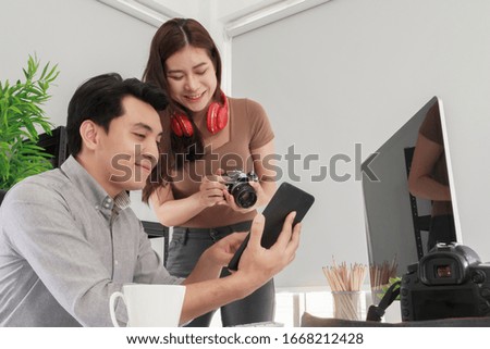 Portrait of Two happy young Asian male photographer and female designer working together, while discussing over computer in a modern office. Creative people, brainstorming, team working concept.
