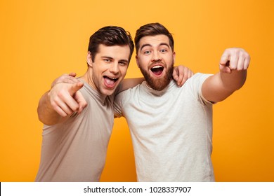 Portrait of a two happy young men pointing fingers at camera isolated over yellow background - Shutterstock ID 1028337907