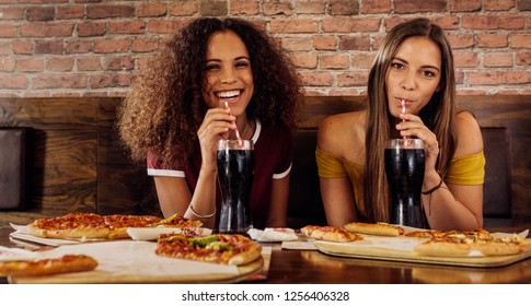 Portrait Of Two Happy Young Women Drinking Soft Drink At Restaurant. Female Friends Having Lunch At Restaurant.