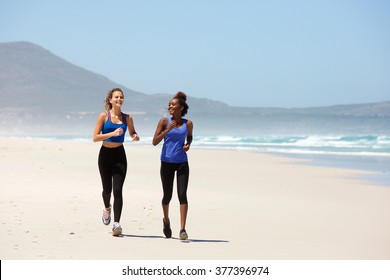 Portrait Of Two Happy Young Women Jogging On The Beach 