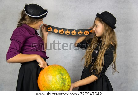 Portrait of two happy young women in black witch halloween costumes over gray background. The concept of Halloween, funny faces. Teenage girls with pictures of pumpkins with different emotions. 
