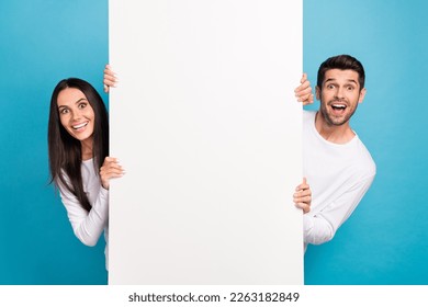 Portrait of two impressed positive people peek behind empty space blank isolated on blue color background