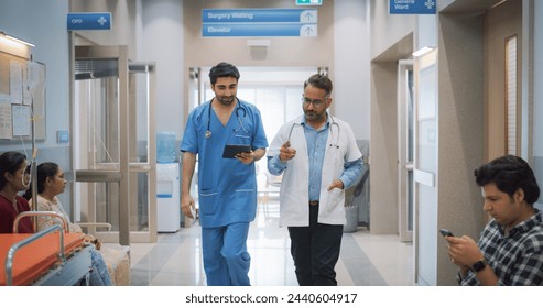 Portrait of Two Indian Male Doctors Walking in Hospital Corridor and Talking while Using a Digital Tablet. Two Medical Specialists Discussing the Treatment of a Patient - Powered by Shutterstock