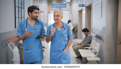 Portrait of Two Indian Male Doctors Walking in Hospital Corridor and Talking while Using a Digital Tablet. Two Medical Specialists Discussing the Treatment of a Patient - Powered by Shutterstock