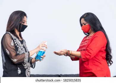 Portrait Of Two Indian Women Wearing Covid 19 Protection Mask, Using Hand Sanitiser To Clean Their Hands, Social Distancing.