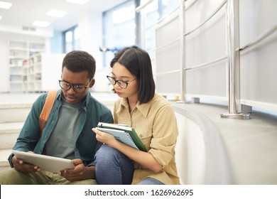 Portrait of two international students reading books together while working on project in modern college library, copy space - Powered by Shutterstock