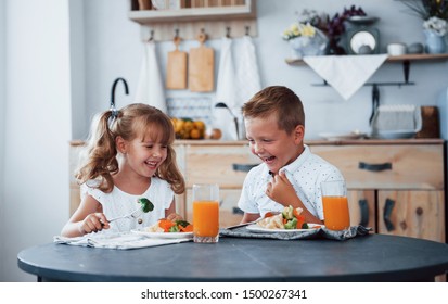 Portrait of two kids in white clothes that have breakfast in the kitchen. - Powered by Shutterstock