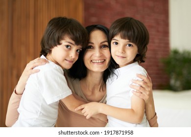 Portrait of two latin children, little twin boys smiling at camera and hugging their mom, spending time together at home