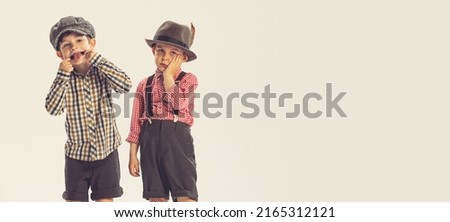 Portrait of two little boys, children in checkered shirts, posing, making funny faces isolated over grey studio background. Concept of childhood, friendship, family, fun, lifestyle, retro fashion