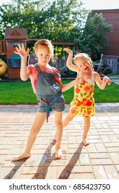 Portrait Of  Two Little Girls  Sisters Having Fun On Home Backyard. Friends Girls Making Silly Faces. Lifestyle Family Moment Of Siblings Playing Together. Real Authentic Moment. 