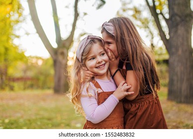 Portrait of two little sisters in a park, whispering secrets. - Powered by Shutterstock