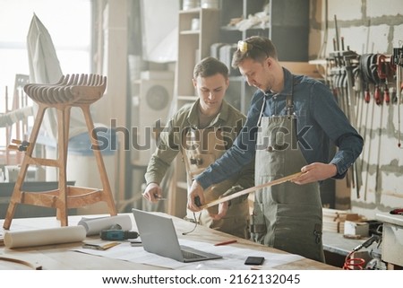 Portrait of two male carpenters building handcrafted wooden furniture in hazy workshop, copy space