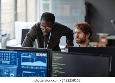 Portrait of two male professionals discussing work issues over computer monitors in cybersecurity office copy space - Powered by Shutterstock