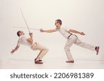 Portrait of two men in a suit fighting with swords isolated over grey studio background. Dynamic image. Concept of sport, hobby, emotions, active lifestyle, retro fashion. Copy space for ad