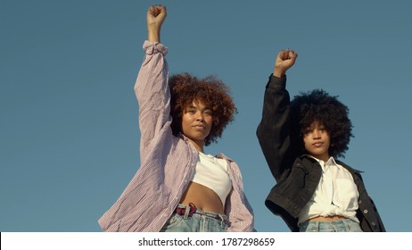 portrait of two mixed-race women with huge afro hair makes a protest black raised fist gesture outdoors portrait on the sky background - Shutterstock ID 1787298659