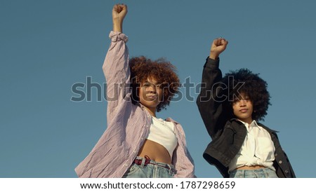 portrait of two mixed-race women with huge afro hair makes a protest black raised fist gesture outdoors portrait on the sky background