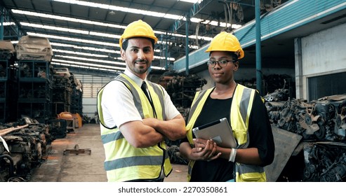 Portrait of two multicultural smiling workers African black female and American male mechanic with safety suit helmet looking camera in old auto parts factory. Industrial workers concept