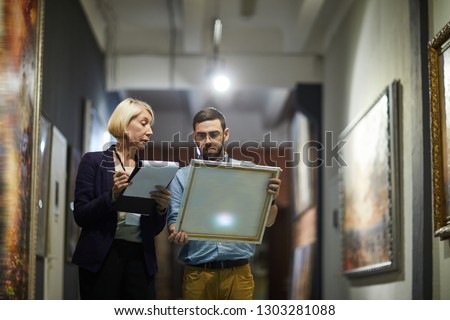 Portrait of two museum workers inspecting paintings standing in art gallery, copy space