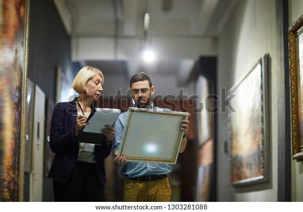 Portrait of two museum workers inspecting\
paintings standing in art gallery, copy\
space