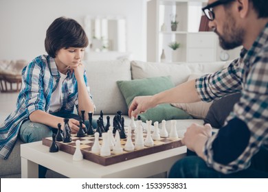 Portrait of two nice skilled focused serious guys dad and pre-teen son sitting on sofa playing chess moving pieces thinking strategy in light white modern interior house living-room - Powered by Shutterstock