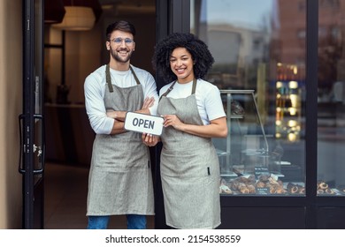 Portrait of two owners friends holding a open sign together while smiling to the camera in front of pastry shop. - Powered by Shutterstock