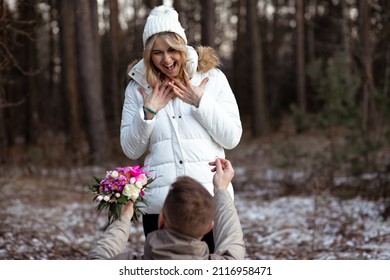 Portrait of two people couple smiling happy woman and man proposal engagement holding bunch of flowers on knees together outdoors. Frost weather. Flowers and forest. Close-up.
