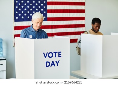 Portrait of two people in voting booths on election day against USA flag, copy space