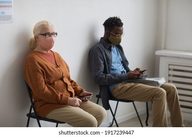 Portrait of two people wearing masks and sitting on chairs while waiting in line at clinic, copy space - Shutterstock ID 1917239447