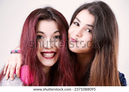 Portrait of two playful young women, possibly sisters or friends, making funny faces. With well-done makeup and long hair, they embrace the silliness of youth and beauty