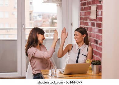 Portrait Of Two Pretty Businesswomen Sitting In Home Office And Giving High Five